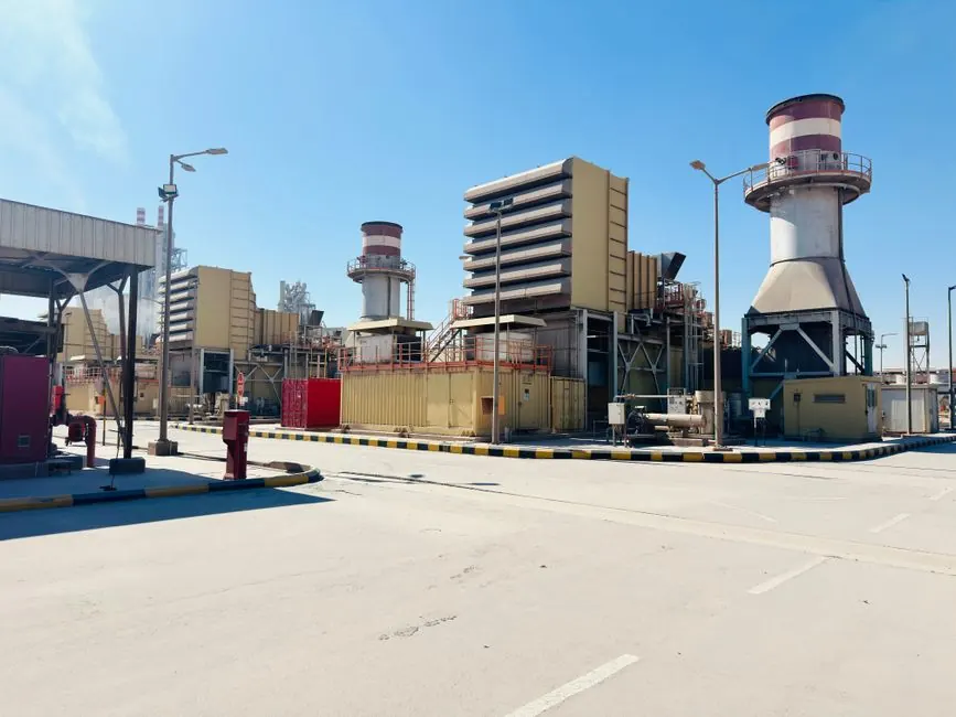 A modern power plant with turbines and chimneys under a clear blue sky in Saudi Arabia.