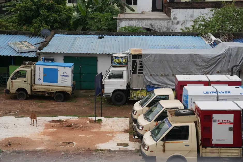 A row of parked utility trucks with generators beside a building outdoors.