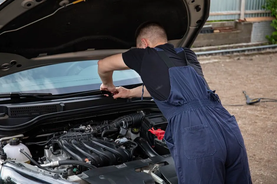 Mechanic fixing car engine outdoors, summer afternoon, skillful work.